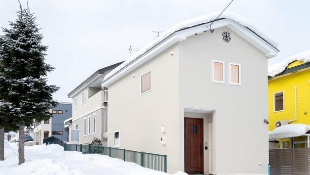 A two-story residential building with a snow-covered roof, a visible front door, and a small porch area. - Rocky-f (Furano)