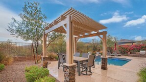Une terrasse couverte avec une piscine, des piliers en pierre et une table entourée de chaises.