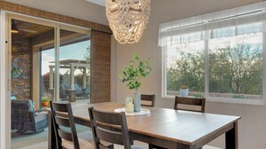 Un coin repas avec une table en bois, des chaises, un lustre et, derrière une porte vitrée, une vue sur un patio extérieur.