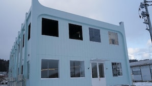 A light blue building with multiple windows, a door, and a small porch area.