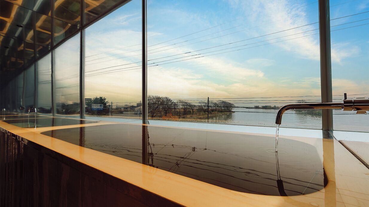 A modern indoor pool with large windows, a wooden deck, and a view of the sky and distant landscape.