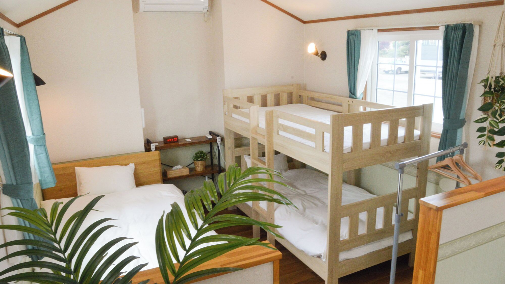 A room with bunk beds, a bedside table with a lamp, a window with curtains, and a plant.