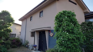 A two-story building with a beige exterior, a black door, and a small window. - Guest House Nodoka (Toyooka)