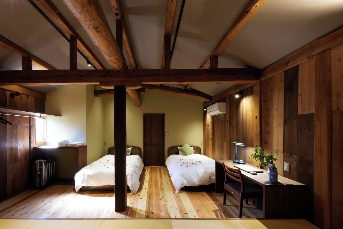 A room with wooden beams, two beds, a desk, and a chair.