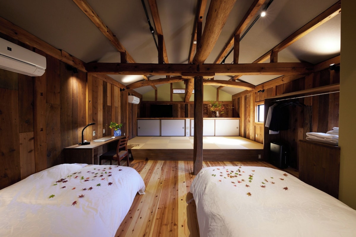 A room with two beds, wooden walls, a kitchenette, and a TV.