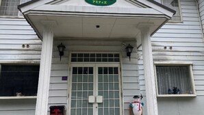 A building with a green sign above the entrance, a white door with glass panels, and a small snowman decoration.