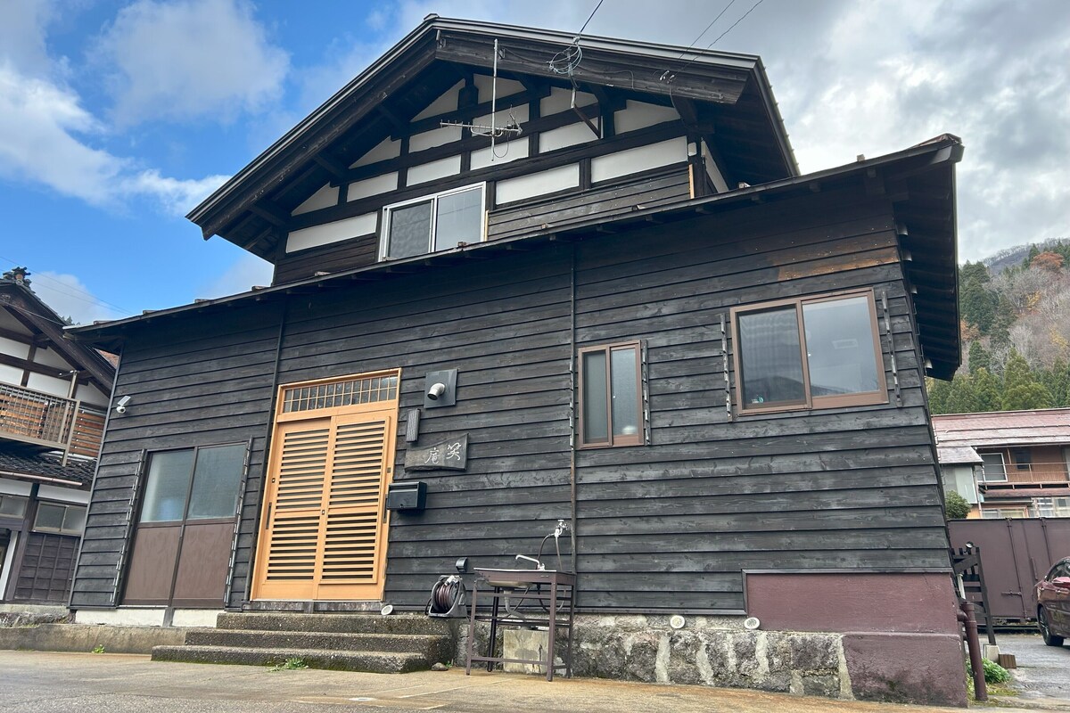 Een traditioneel houten huis met een schuin dak, een houten deur en een klein portaal.