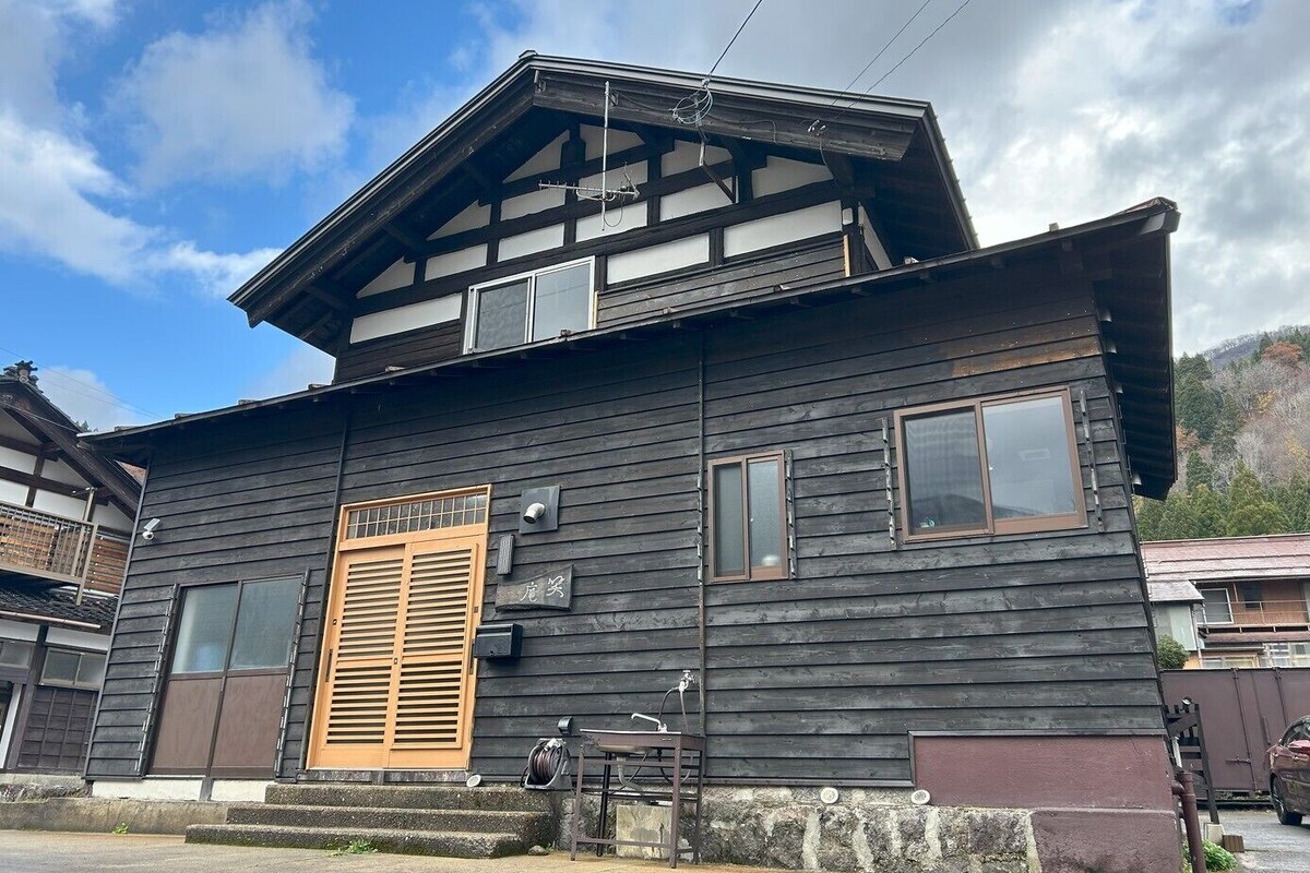 Een traditioneel houten huis met schuin dak, een houten deur en een klein portaal.