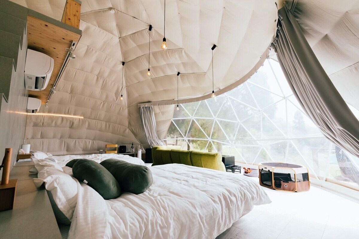 A modern, spacious bedroom with a large bed, a wooden shelf, and a geometric window design.