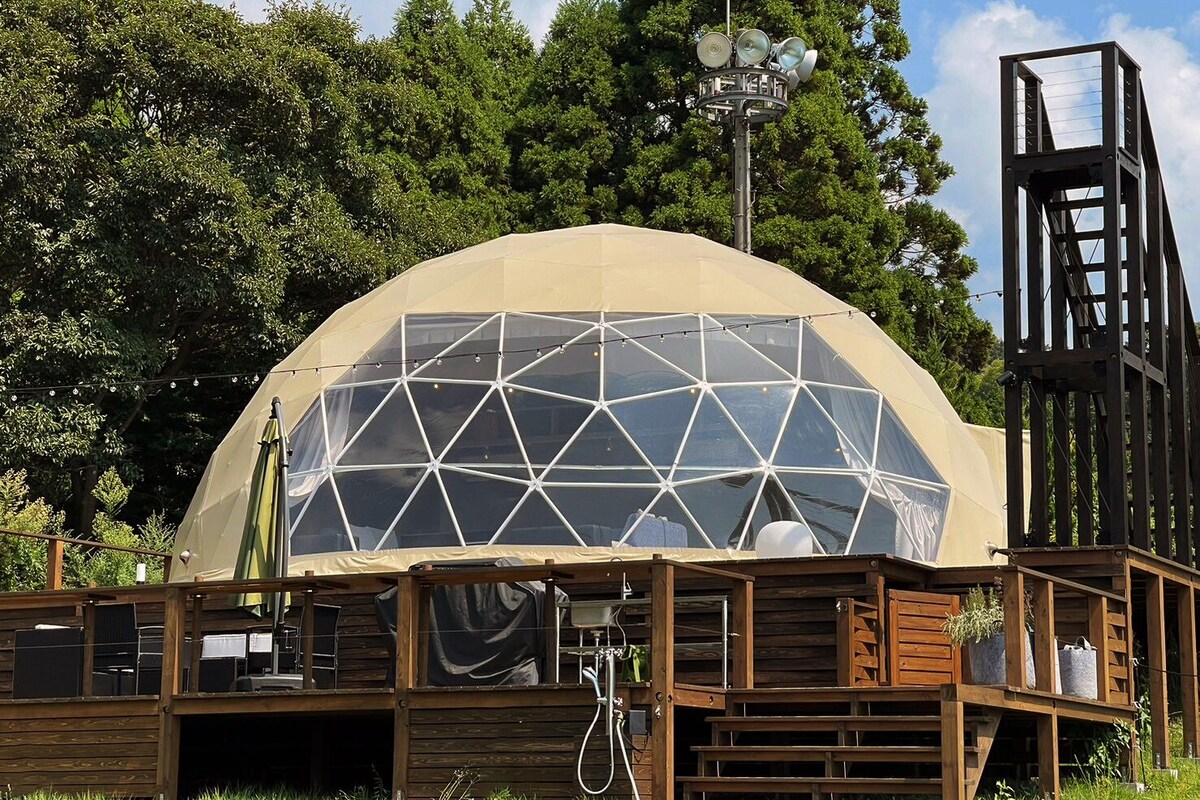 A geodesic dome structure with a wooden deck and a metal tower.