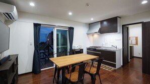 A modern kitchen with a dining area, a TV, and a sliding glass door leading to an outdoor space. - Code Rooms Okinawa (Nakijin)