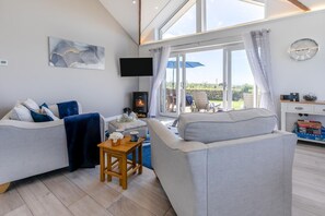 Ein modernes Wohnzimmer mit zwei Sofas, einem Fernseher, einem Kamin und Blick ins Freie.
