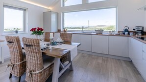 Une cuisine moderne avec un coin repas, de grandes fenêtres et une vue sur la campagne.