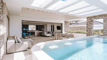 A modern outdoor pool area with a stone wall, a seating area with a sofa and chairs, and a dining table.