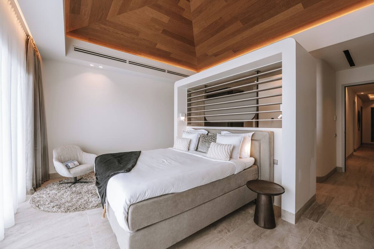 A modern bedroom with a large bed, a chair, a small table, and a built-in shelf.