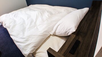 A neatly made bed with white bedding and a pillow, a wooden headboard, and a dark blue wall.