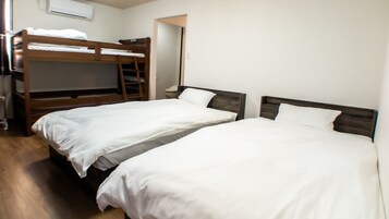 A room with two single beds, a bunk bed, a wooden desk, and a chair.