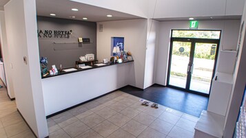 A hotel reception area with a counter, a clock, and a door leading outside.