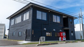 A two-story building with a dark exterior, large windows, and a Coca-Cola vending machine on the ground floor.