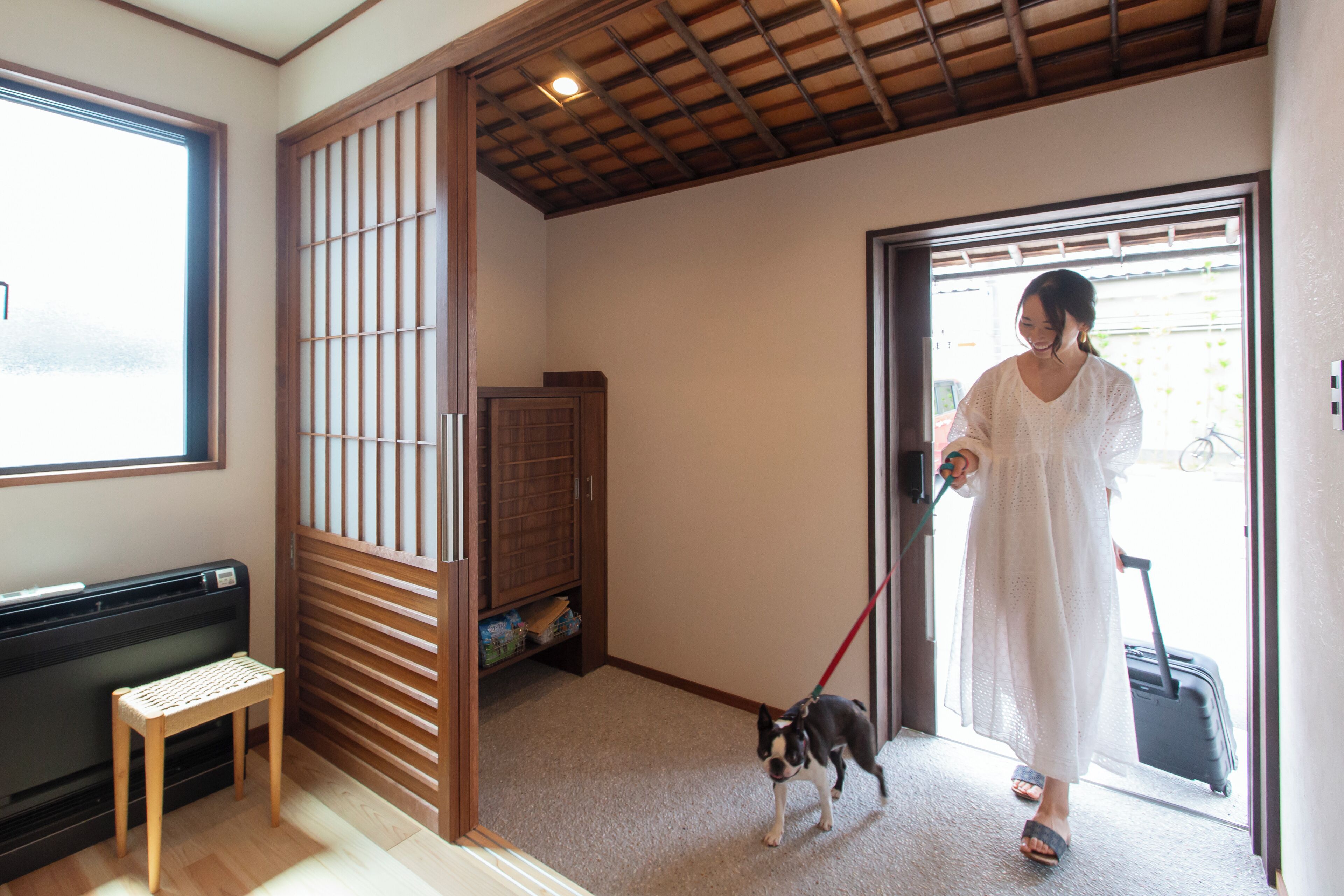 A room with a sliding door, a bench, a dog on a leash, and a person with a suitcase.