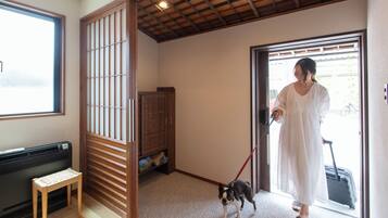 A room with a sliding door, a bench, a dog on a leash, and a person with a suitcase.