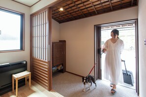A room with a sliding door, a bench, a dog on a leash, and a person with a suitcase. - Yado no Kura Hug (Matsue)
