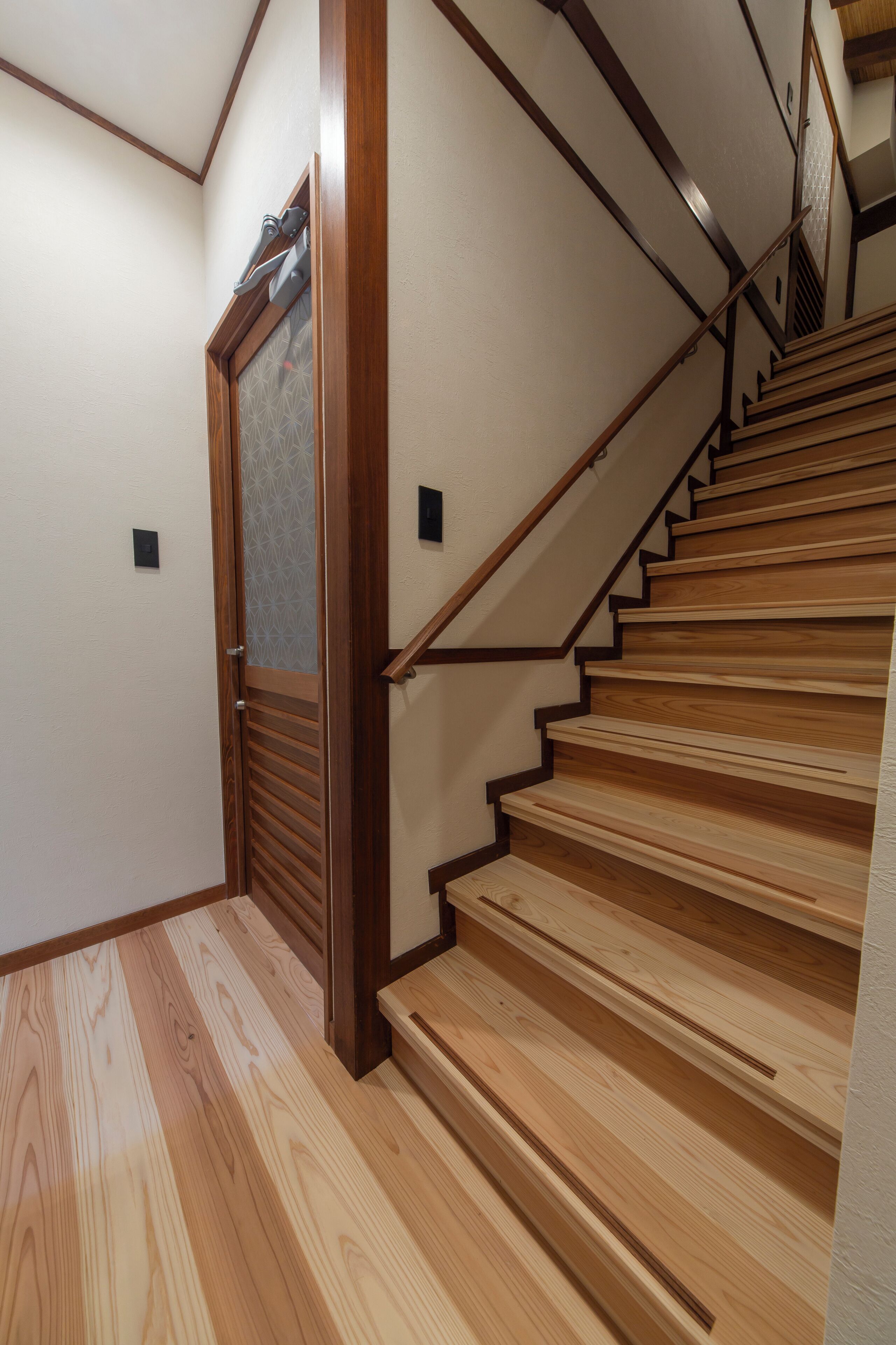 A wooden staircase with a handrail and a door with a patterned glass panel.