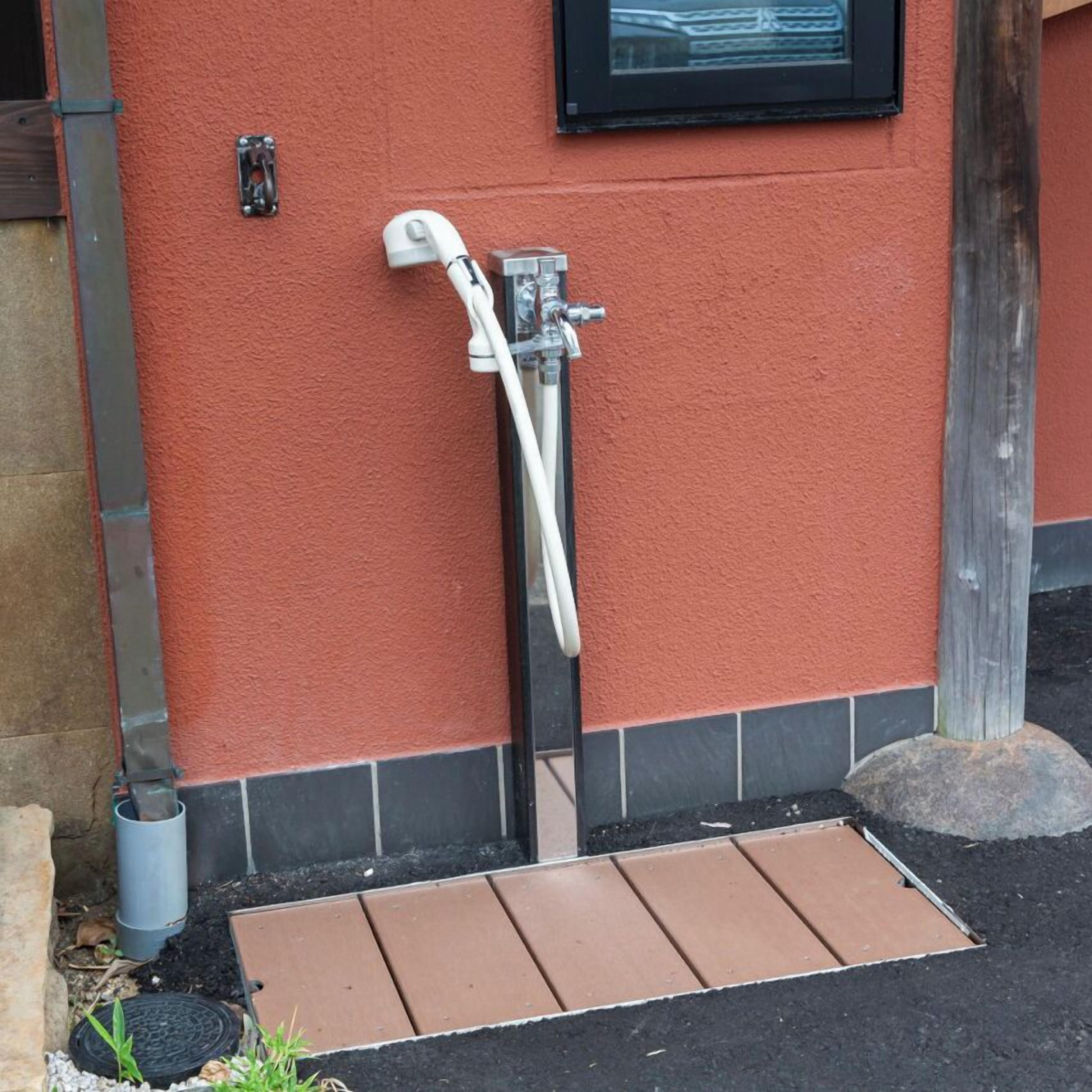 A red exterior wall with a white outdoor shower, a small window, and a metal door frame.