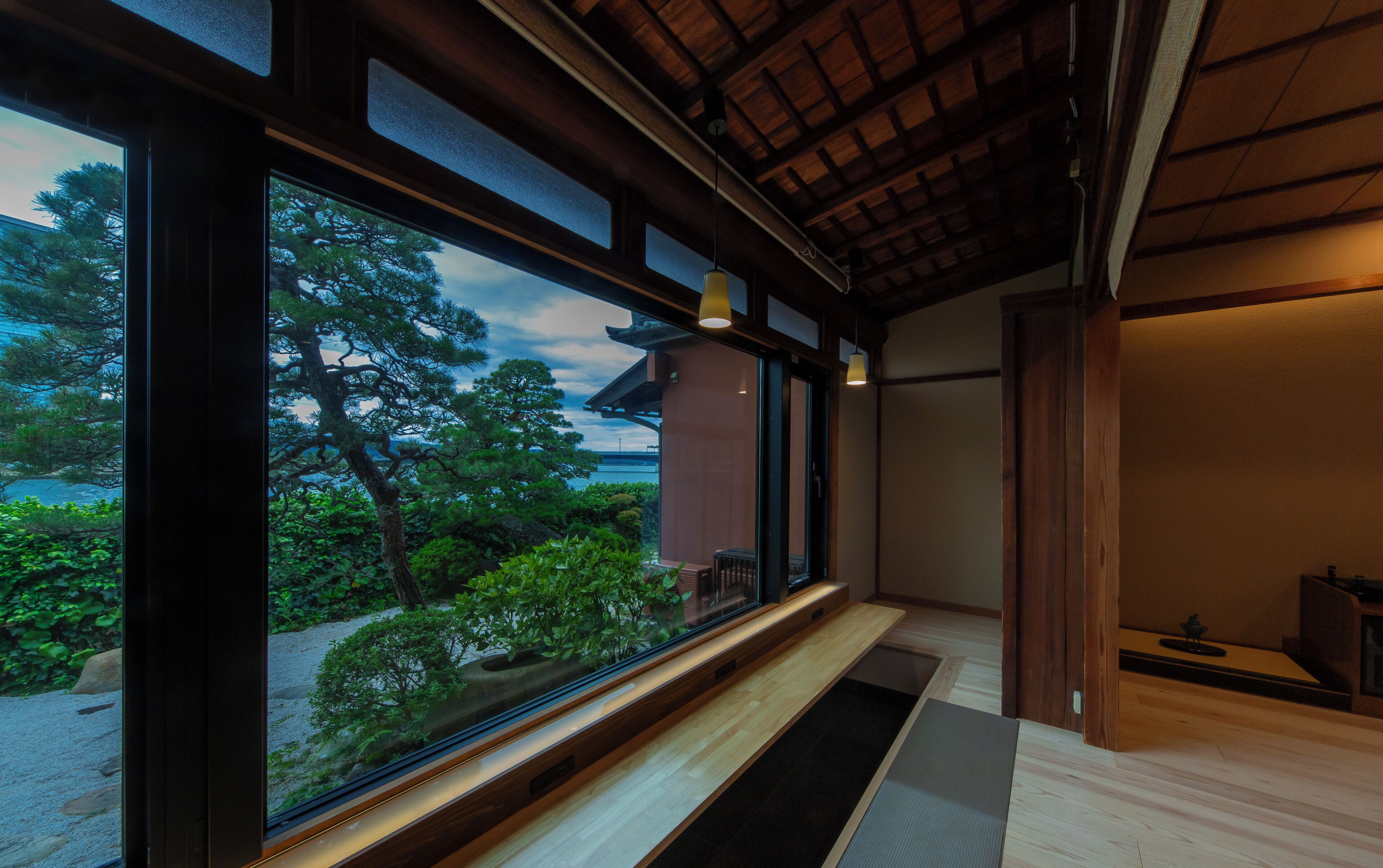 A room with large windows, a wooden bench, and a view of a tree and sky.