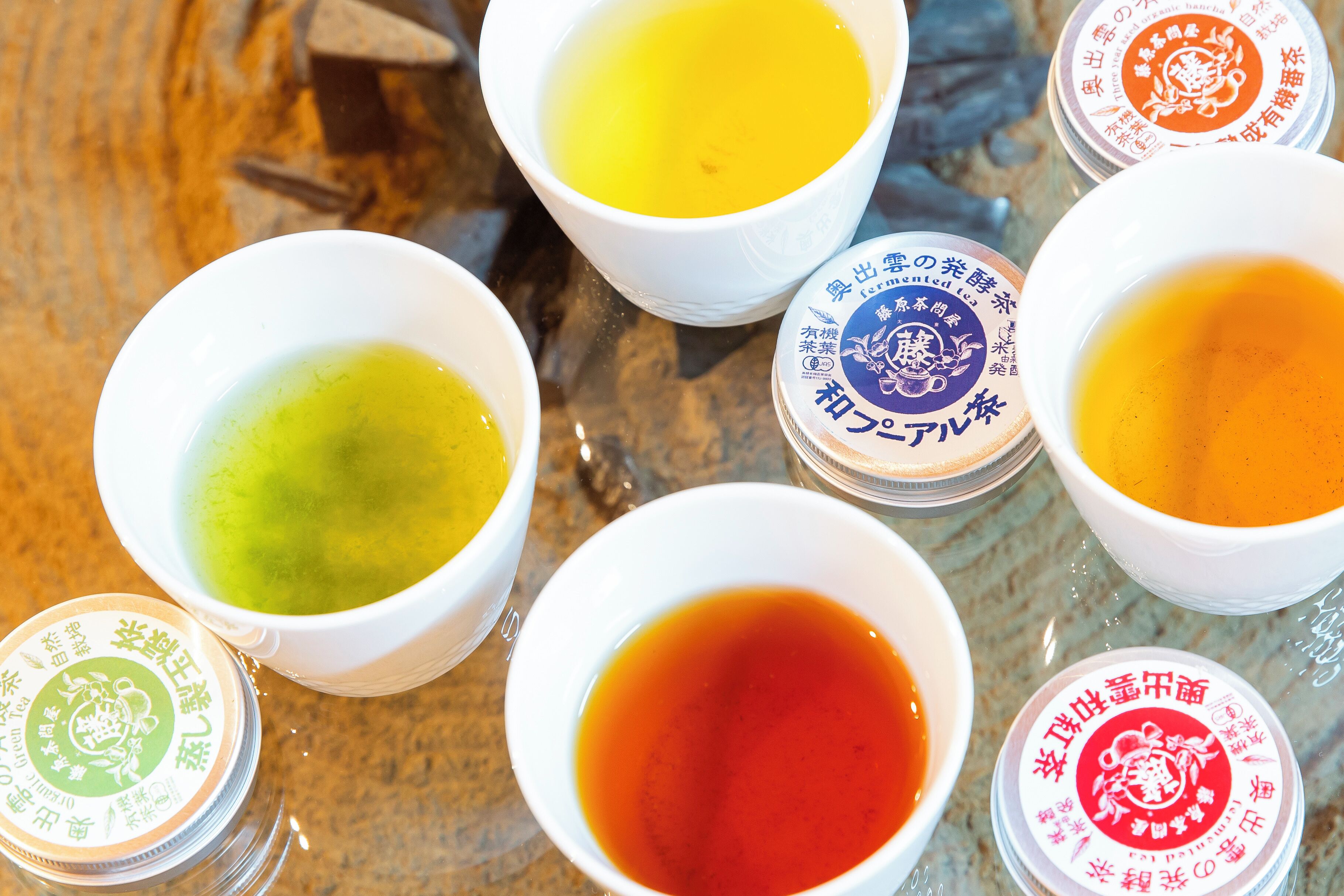 A table with several white bowls containing different colored liquids, each with a lid featuring Japanese text.