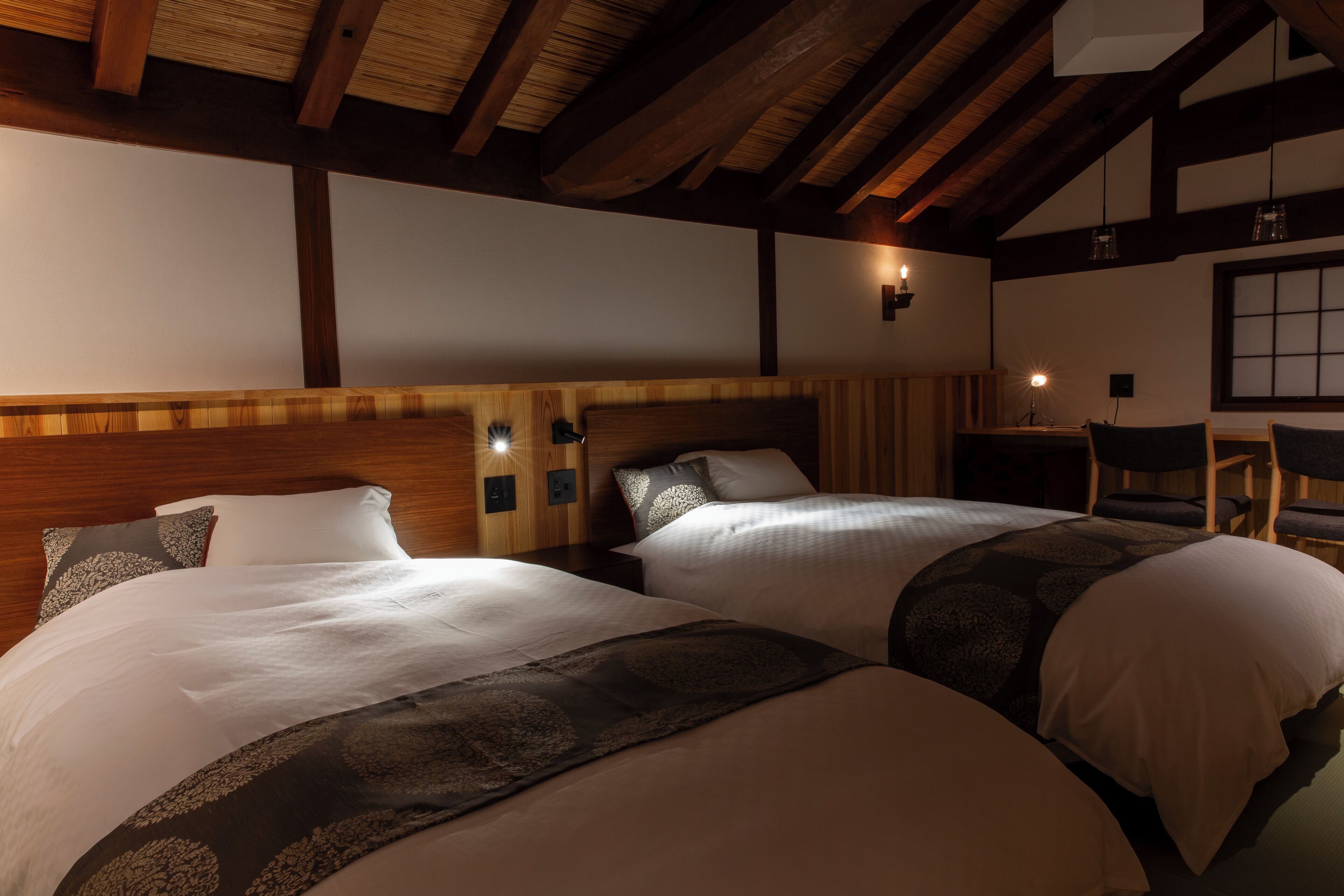 A hotel room with two beds, wooden beams, a nightstand, and a chair.