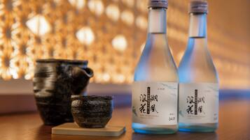 Zwei Flaschen Sake mit Etiketten, eine Keramiktasse und eine kleine Schale auf einer Holztischfläche.