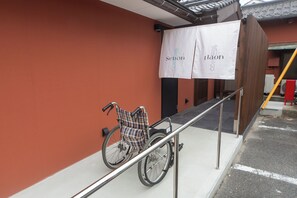 Un fauteuil roulant est garé à côté d’une rambarde, de l’entrée d’un bâtiment et d’une banderole avec du texte.