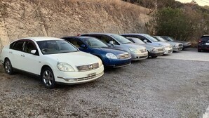 A row of parked cars on a gravel surface with a rocky hillside in the background. - Kurinoyakata (Kunisaki)