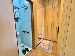 A small bathroom with a shower, toilet, and a wooden door. - Coco House (Ishigaki)
