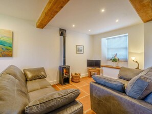 Una sala de estar acogedora con chimenea, sofás de cuero, televisor y ventana con persianas.