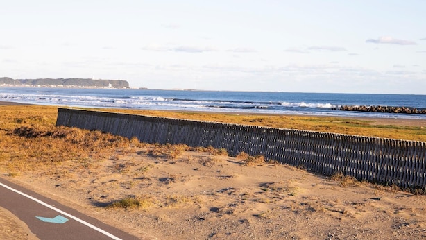 Una carretera costanera amb una tanca de fusta, cel serè i l'oceà al fons.