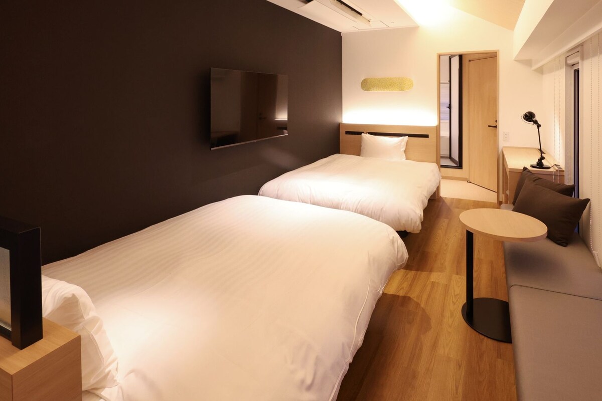 A hotel room with two beds, a TV, a small table, and a sofa.