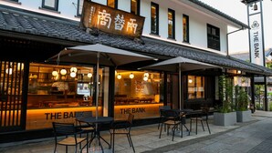 Um restaurante com mesas ao ar livre, uma placa com a inscrição 'THE BANK' e um telhado tradicional japonês.