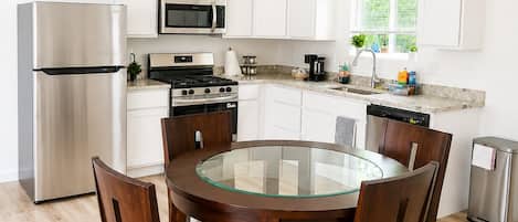 A modern kitchen with white cabinets, stainless steel appliances, a glass-top dining table, and wooden chairs.