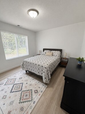 Une chambre à coucher comprenant un lit, des tables de chevet, une commode, un bureau, une plante en pot et un tapis à motifs.