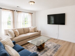 Un salon avec un canapé, une table basse, un téléviseur et une fenêtre avec des rideaux.
