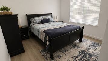 Une chambre à coucher comprenant un lit, des tables de chevet, une armoire, une fenêtre avec des stores et un tapis à motifs.