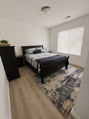 Une chambre à coucher comprenant un lit, des tables de chevet, une armoire, une fenêtre avec des stores et un tapis à motifs.