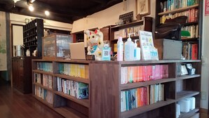 Una librería con estanterías de madera llenas de libros, una computadora portátil en el mostrador y una estatua decorativa de un gato.
