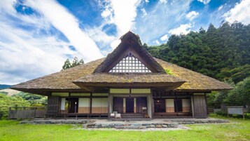 Una casa tradicional japonesa con techo de paja, fachada de madera y un sendero de piedra que lleva a la entrada.