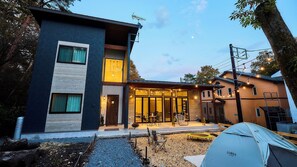 A modern two-story building with a covered patio area, a tent, and a gravel driveway. - Troll Forest Stella (Nikko)