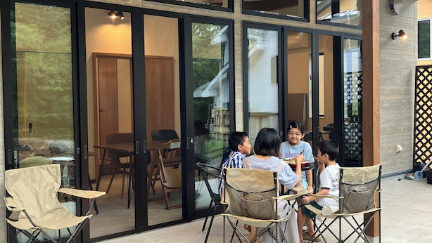 An outdoor dining area with a glass wall, wooden chairs, and a ceiling fan. - Troll Forest Stella (Nikko)