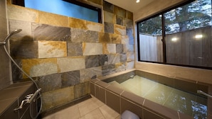 A bathroom with a stone wall, a bathtub, and a shower. - Troll Forest Stella (Nikko)
