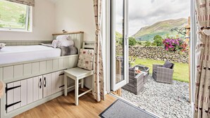 A bedroom with a bed, a small table, and a view of a stone wall and greenery outside. - 1 Bed in Penrith (oc-85532) (Deepdale)
